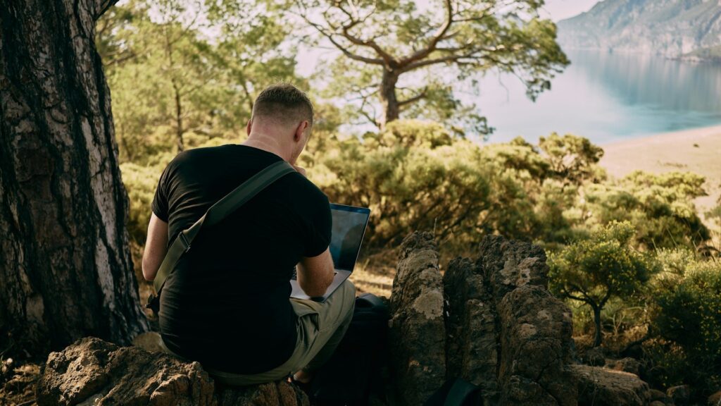 Persoon werkt anoniem op laptop in natuur, passend bij online anonimiteit en werken zonder herkenbare identiteit
