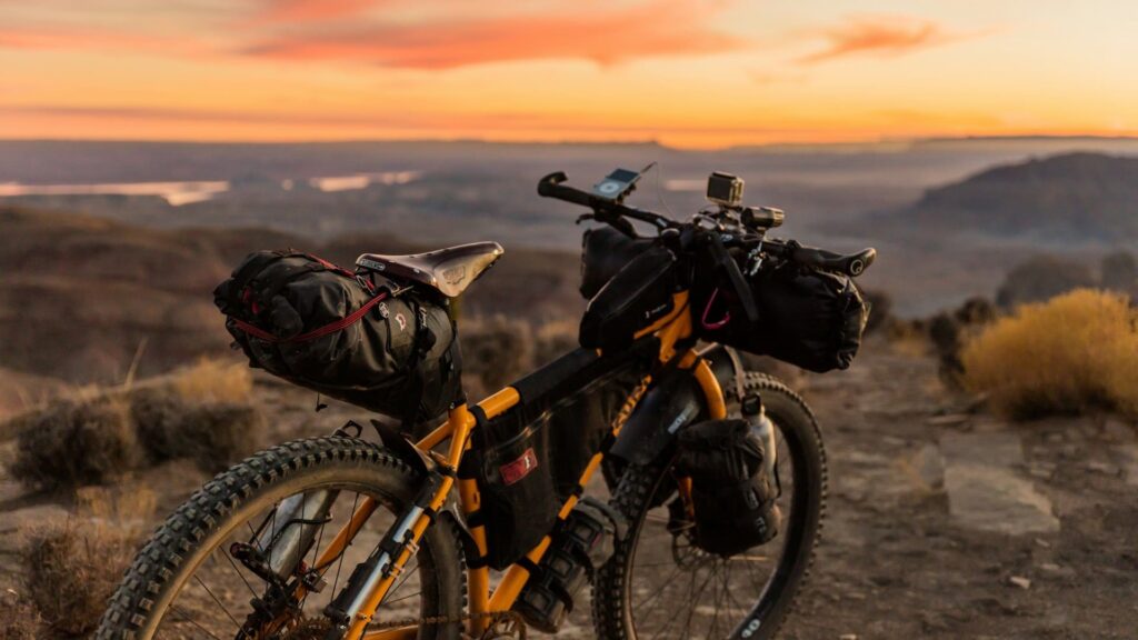 Fiets leasen voor avontuur: gele mountainbike met bepakking op bergpad bij zonsondergang.