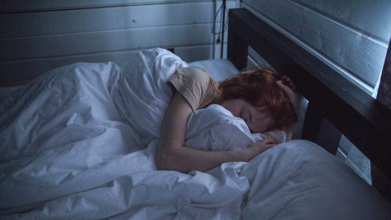 Vrouw ligt rustig te slapen in een donker ingerichte slaapkamer, passend bij tips voor beter slapen