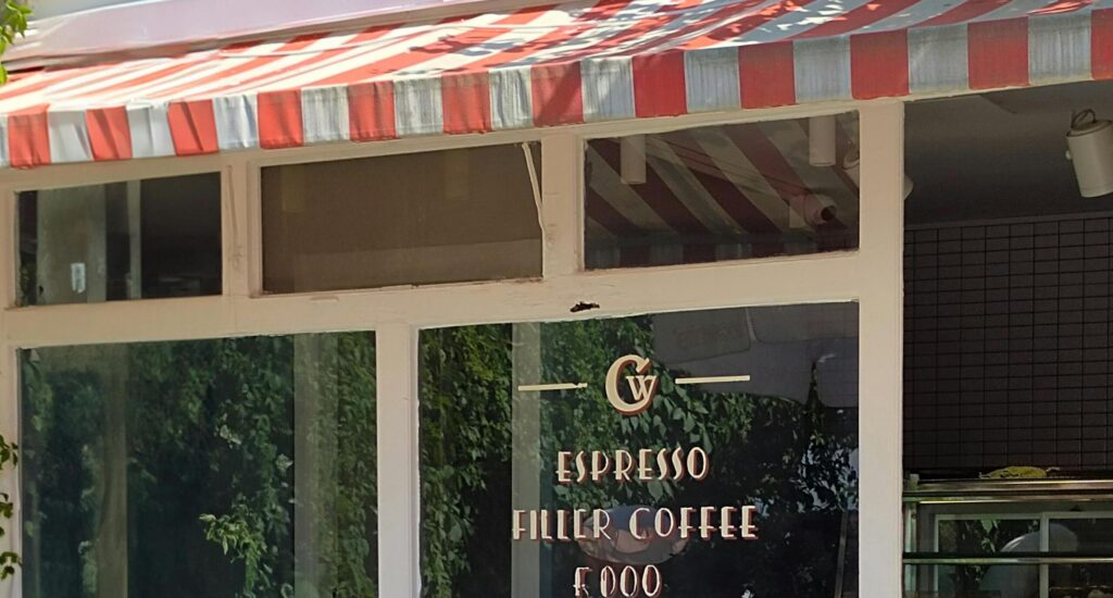 Gevel van koffiebar met rood-wit gestreepte luifel en tekst “Espresso Filter Coffee” op raam