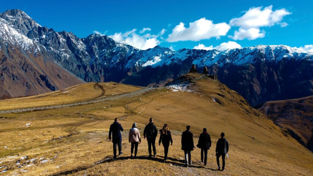 Groep jongeren reist na je studie door berglandschap met uitzicht op besneeuwde bergen en een kerk op een heuvel