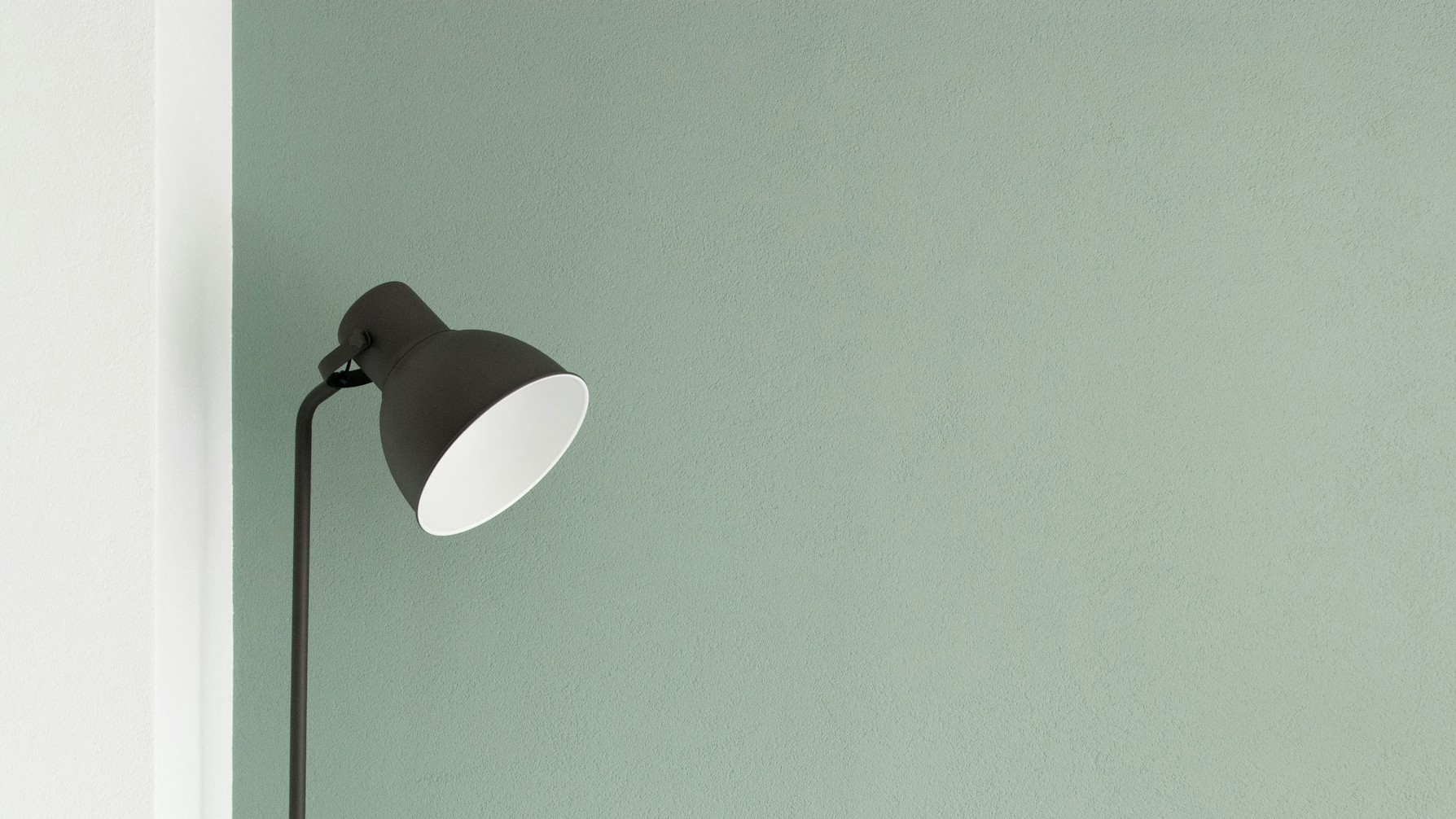 Minimalistische zwarte vloerlamp tegen een rustige, lichtgroene muur als voorbeeld van een kalme inrichting